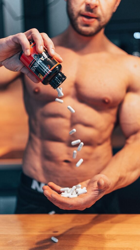 pexels-photo-15120890-15120890 Shirtless man pouring white supplement capsules into his hand with muscles in focus.