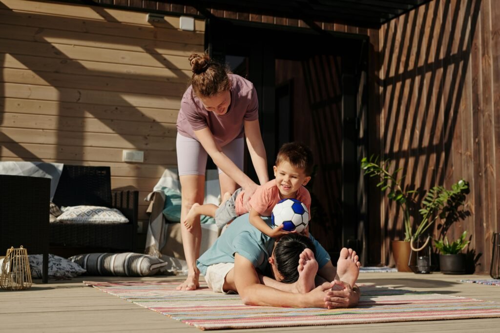 pexels-photo-5445215-5445215 Family engaging in playful yoga on a sunlit porch, bonding and exercising together.