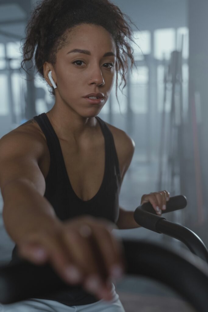 African American woman exercising on a stationary bike indoors with earphones. Fitness and concentration.