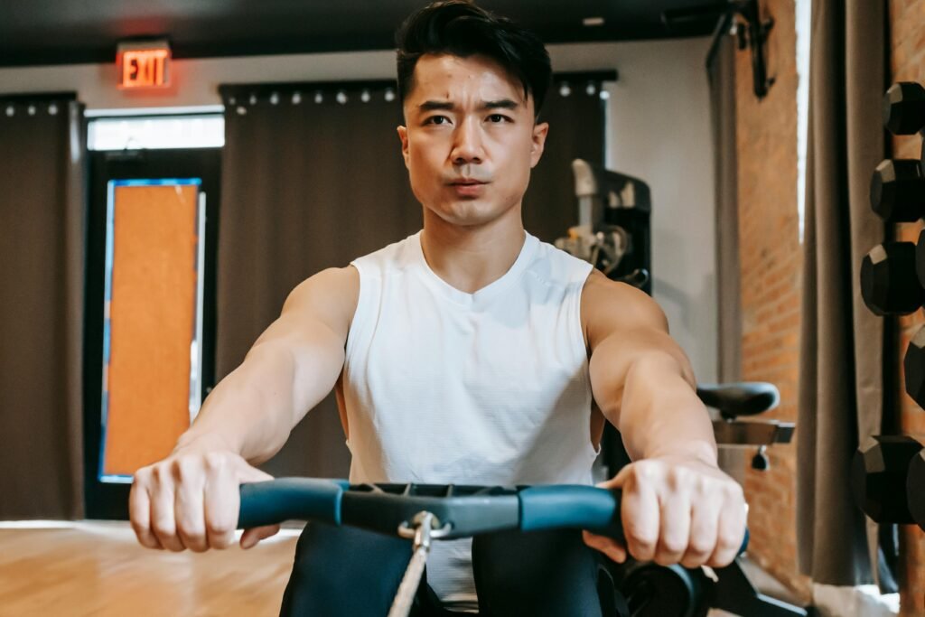 pexels-photo-6551061-6551061 Young Asian man performing a rowing workout in a gym, concentrating on fitness and endurance.
